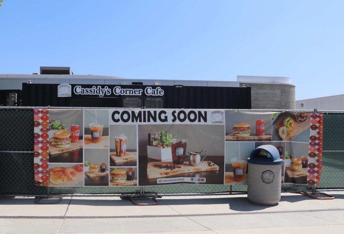 A sign advertising that the Cassidy's Corner Cafe at Cerritos College is coming soon. The advertisement is placed on the fence where the cafe will be once it's back. 