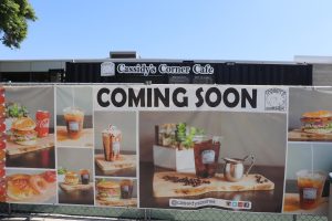 A sign advertising that the Cassidy's Corner Cafe at Cerritos College is coming soon. The advertisement is placed on the fence where the cafe will be once it's back.