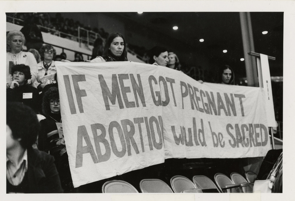 Women Holding Banner, “If Men Got Pregnant Abortion Would be Sacred” at the National Women’s Conference. Photo credit: The U.S. National Archives